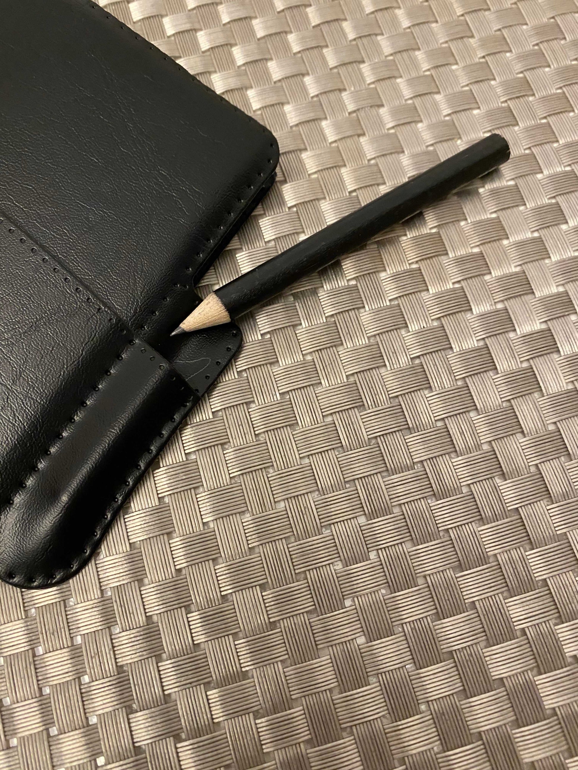 Black wooden apple pencil apple with pointed tip next to black leather case on woven surface